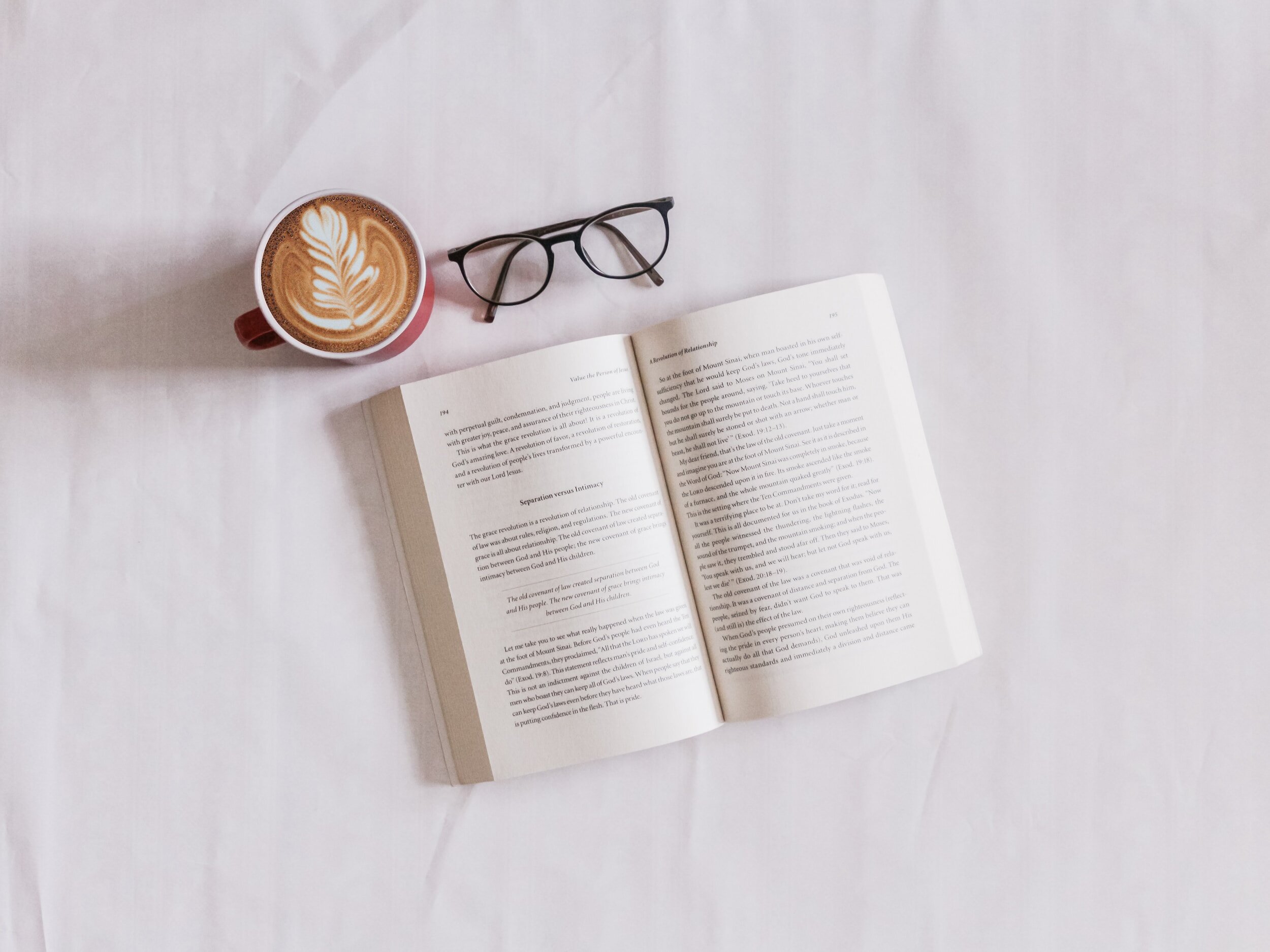 A coffe cup, reading glasses and book on a layflat.